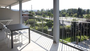 Un balcone con tavolo e sedie, vista su una strada e vegetazione.