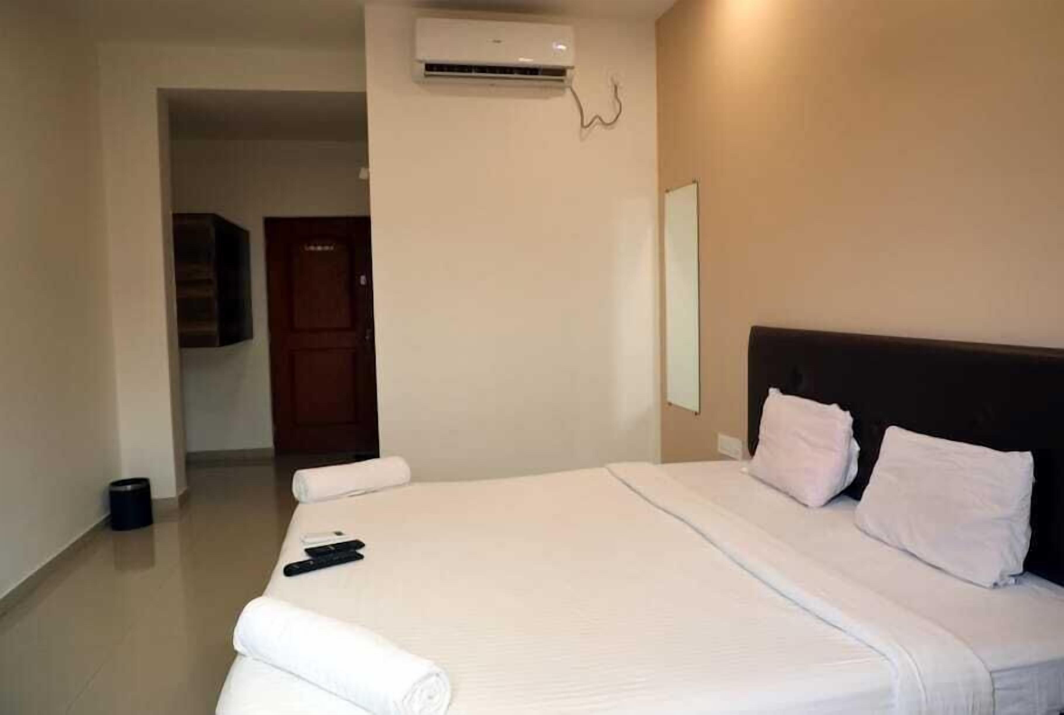 A hotel room with a large bed, a flat-screen TV mounted on the wall, and an air conditioning unit above the bed.
