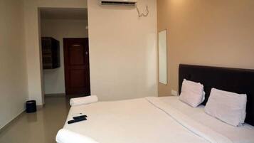 A hotel room with a large bed, a flat-screen TV mounted on the wall, and an air conditioning unit above the bed.