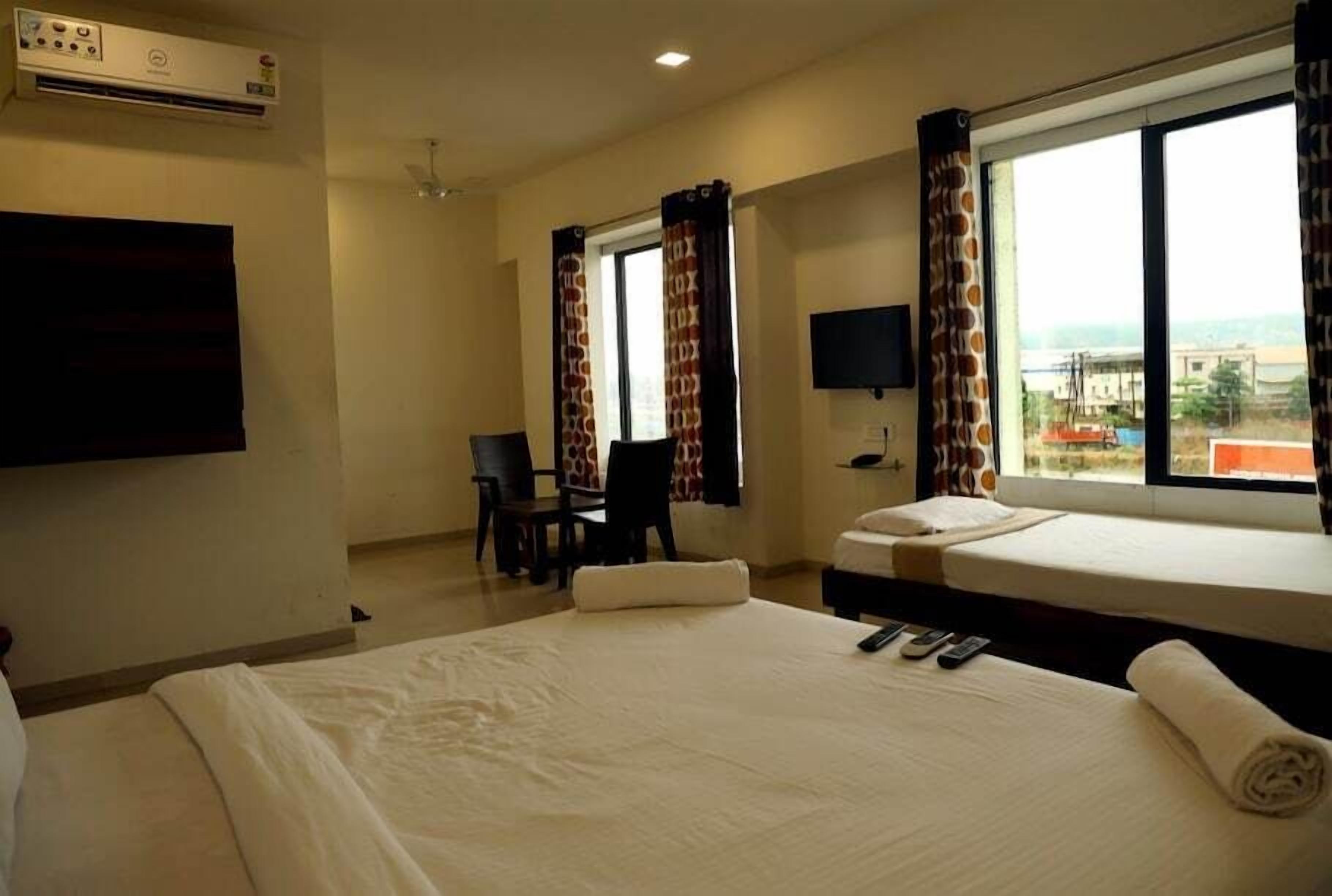 Habitación de hotel con una cama grande, un escritorio con silla, un televisor en la pared y una ventana con cortinas.