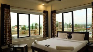 Quarto de hotel com uma cama grande, uma mesa pequena e vista para a cidade através de amplas janelas.