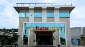 Um hotel chamado Krushna Express com fachada moderna, grandes janelas e uma placa indicando quartos disponíveis.