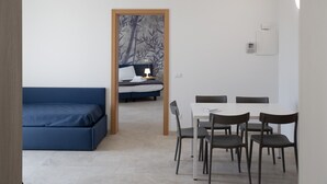 A room with a blue sofa, a dining table with chairs, and a bed with a nightstand. - Deluxe Suite 2 with Shared Pool and Private Balcony (Manerba del Garda)