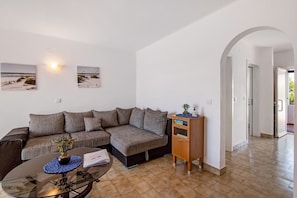 Un salon comprenant un canapé, une table basse en verre, un meuble en bois et deux tableaux accrochés au mur.