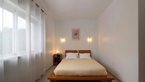Une chambre à coucher avec un lit en bois, des rideaux blancs, une table de chevet avec une lampe et un luminaire fixé au mur.