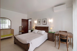A bedroom with a bed, a wooden desk, a chair, a crib, and a wall-mounted air conditioner.