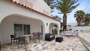 Une terrasse extérieure avec un sol en pierre, une table et des chaises, et un palmier.