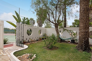 A courtyard with a tennis court, a white wall with circular windows, and a hammock.