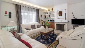 Un salon comprenant un canapé, des fauteuils, une table basse, un téléviseur, une cheminée et des objets décoratifs disposés sur des étagères.