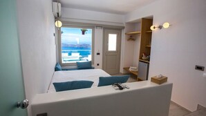 A bedroom with a bed, a bedside table, a wardrobe, and a view of the sea. - Caldera's Majesty (Santorini)