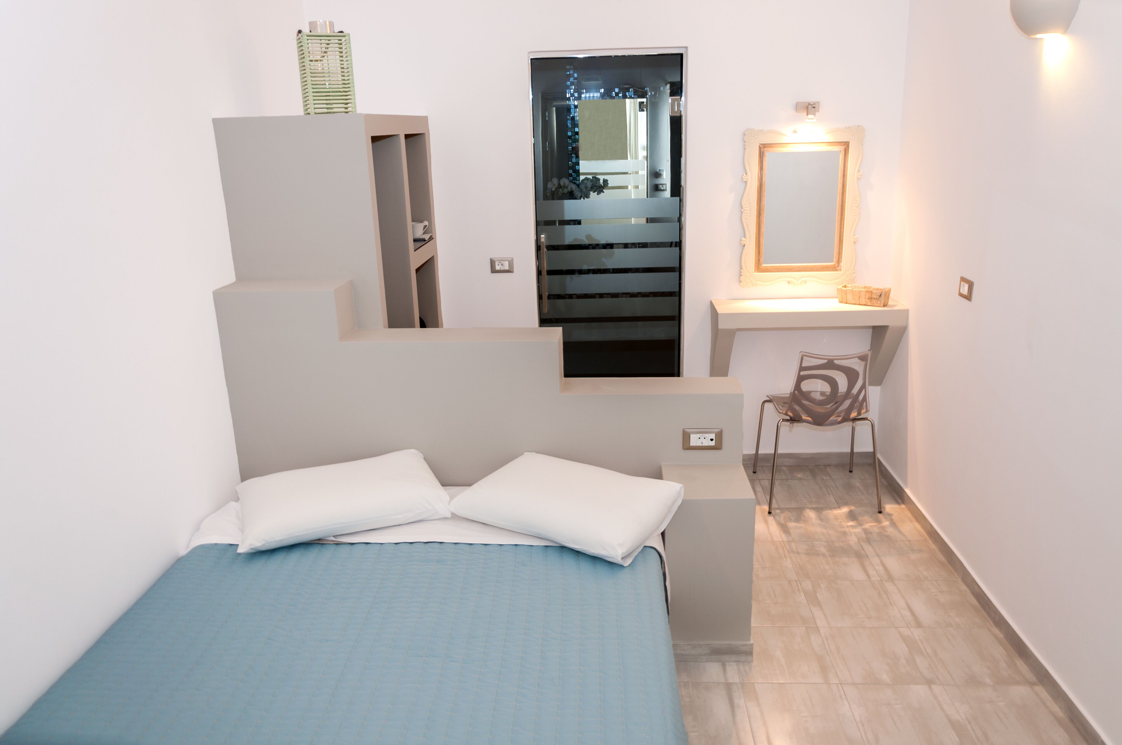 A bedroom with a bed, a chair, a mirror, and a staircase leading to an upper level.