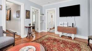 Uma sala de estar com televisão de tela plana na parede, mesa de centro de madeira, tapete estampado e poltrona cinza.