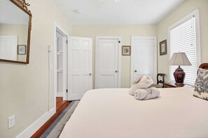 A bedroom with a bed, a nightstand, a lamp, a vase, and a window with blinds. - Pet Friendly | Downtown Mystic Family Retreat (Mystic)