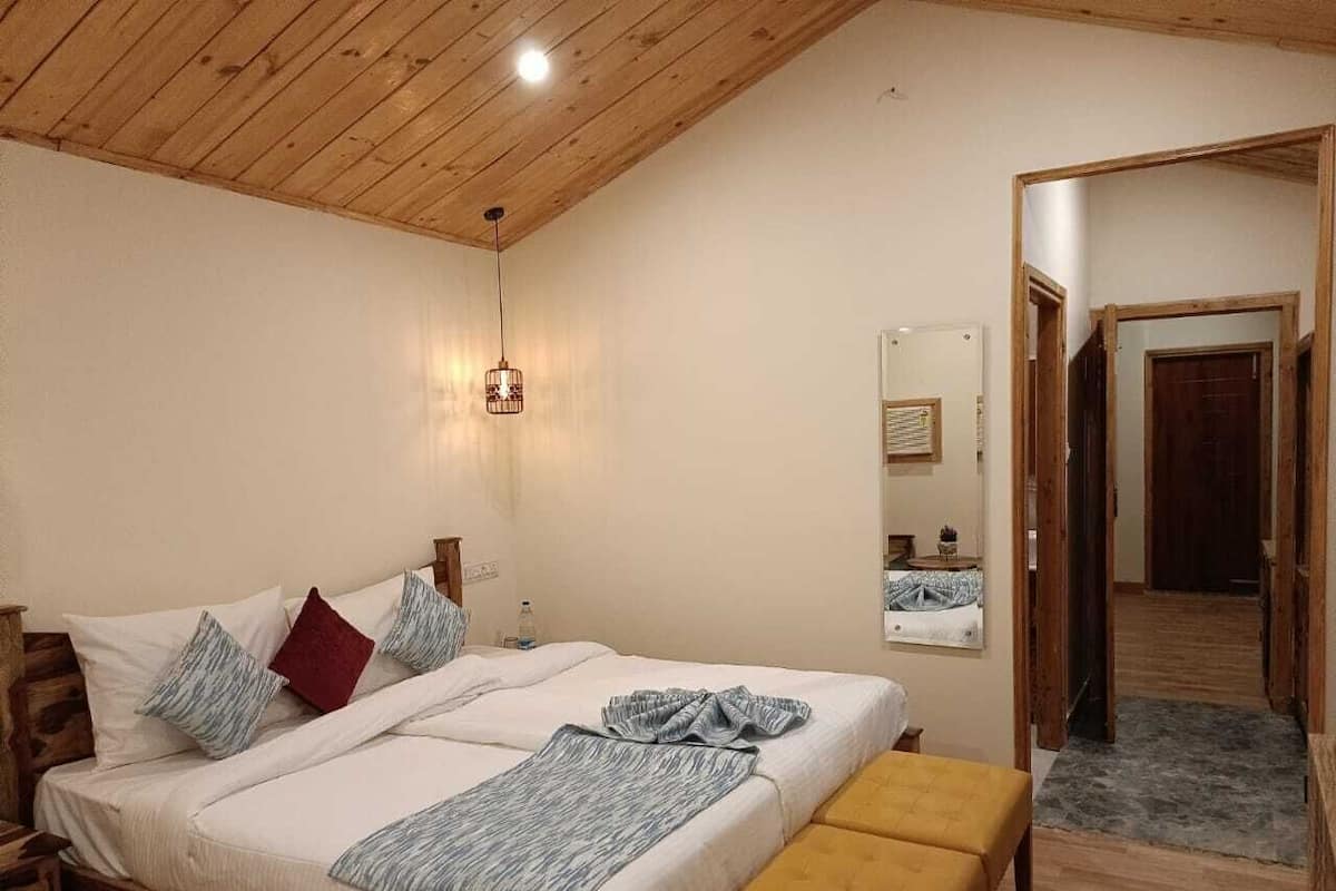 A bedroom with a wooden ceiling, a bed with white bedding and pillows, a bedside table, and a mirror on the wall.