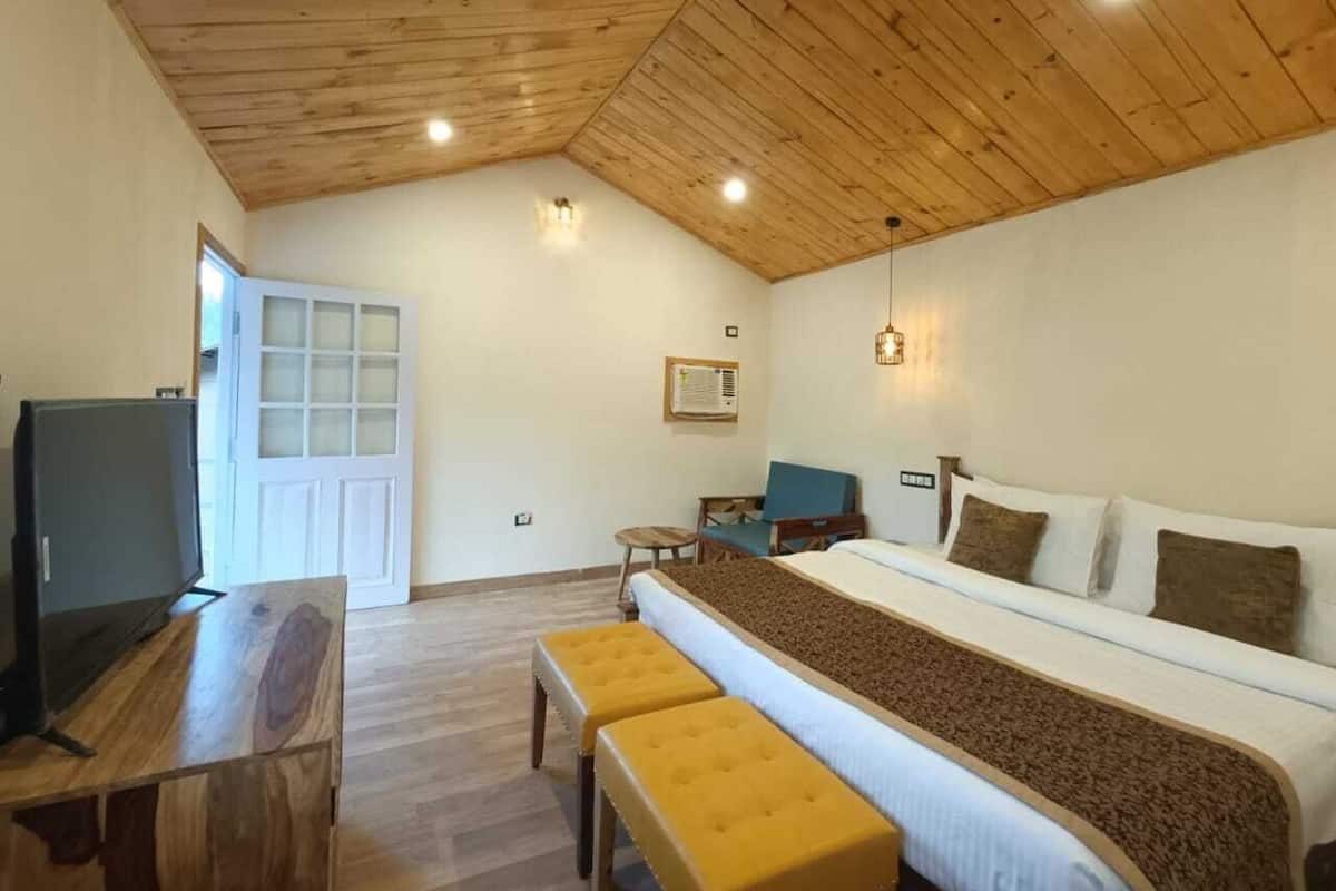 A room with a wooden ceiling, a bed with a brown blanket, a TV on a wooden table, and a door with frosted glass panels.