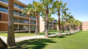 Een hotel met meerdere verdiepingen, palmbomen en een verzorgd gazon.