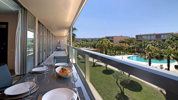 Een balkon met een eettafel voor vier personen, met uitzicht op een zwembad en palmbomen.