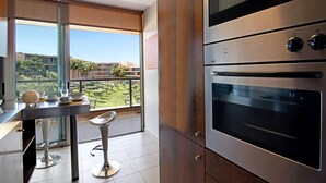 Een moderne keuken met roestvrijstalen apparatuur, een eethoek met een glazen tafel en barstoelen, en een balkon met uitzicht op de stad.