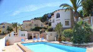 Zwembad met ligbedden, omringd door gebouwen in mediterrane stijl, palmbomen en een heldere lucht.