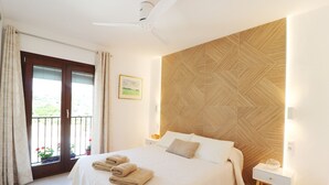 A hotel room with a bed, a nightstand, a wall-mounted light, a ceiling fan, a window with curtains, and a view of greenery outside. - 1130 Casa Antana (Frigiliana)