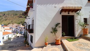 A white building with a wooden door, potted plants, and a cobblestone street. - 1130 Casa Antana (Frigiliana)