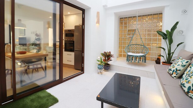 A modern living space with a glass door leading to a kitchen, a black coffee table, a sofa with patterned cushions, and a potted plant. - 1130 Casa Antana (Frigiliana)