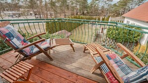 Ett trädäck med två solstolar, ett grönt metallräcke och utsikt över ett bostadsområde med träd och ett hus.