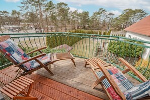 A wooden deck with two lounge chairs, a green metal railing, and a view of a residential area with trees and a house. - Apartment (Seebad Ahlbeck)