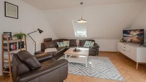 Ett modernt vardagsrum med en brun lädersoffa, ett vitt soffbord och en bokhylla.