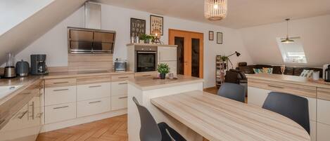 A modern kitchen with a central island, a dining area, and a loft bedroom with a skylight.