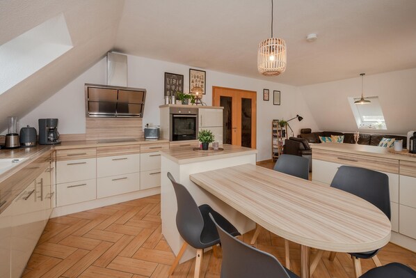 Una cocina moderna con una isla central, un comedor y un dormitorio entre desniveles con tragaluz.