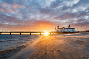 A beach with a pier and a building with two domes. - Apartment (Seebad Ahlbeck)