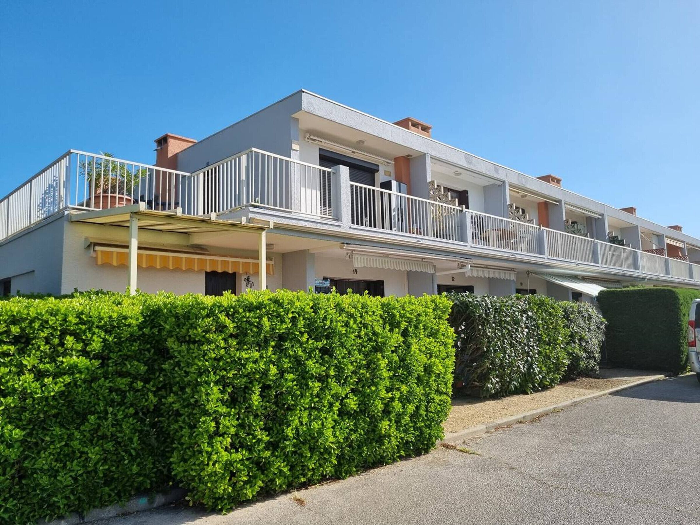 A multi-story residential building with balconies, a covered entrance, and a well-maintained hedge in front.