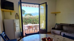 A room with a dining table, chairs, a sofa, and a refrigerator. - Ground-Floor Studio Cabin for 4 with Terrace – 300m from Beach & Shops (Argelès-sur-Mer)