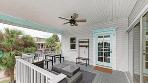 A covered porch with a ceiling fan, a table with chairs, and a door with glass panels. - Aloha Fern: North End Beach House, Pool by Anna Maria Life Vacation Rentals (Anna Maria)