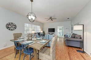 A modern living room with a dining area, a grey sofa, a TV, and a clock on the wall.