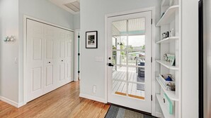 A hallway with a white door, a framed picture on the wall, and a view of a deck outside. - Aloha Fern: North End Beach House, Pool by Anna Maria Life Vacation Rentals (Anna Maria)