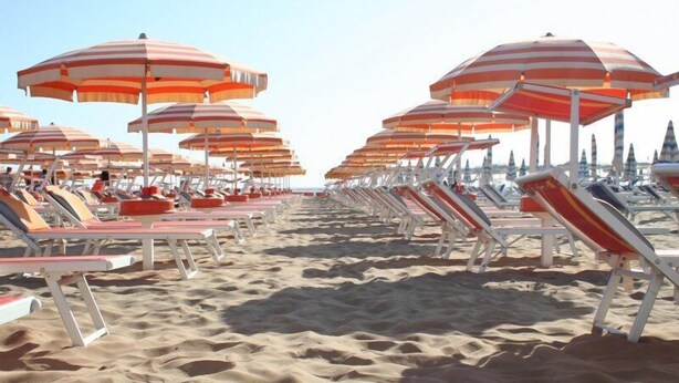 A beach with rows of sun loungers and striped beach umbrellas.