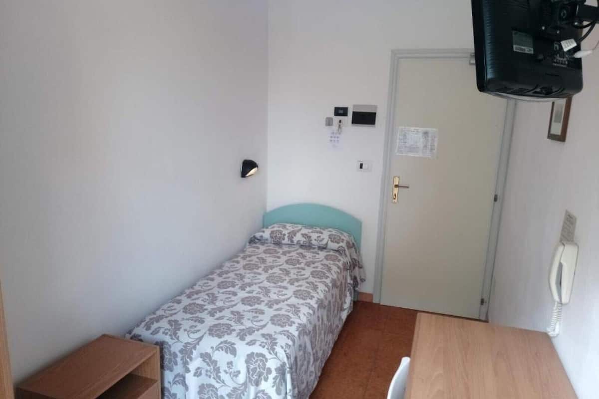 Een kleine eenpersoonskamer met een houten bureau, een tv aan de muur en een deur met een telefoon.