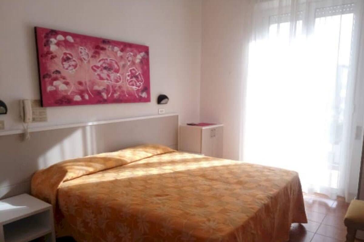 Een slaapkamer met een bed, een nachtkastje, een klein kastje en een raam met gordijnen.