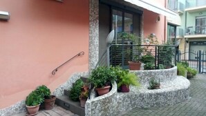 A building with a stone staircase leading to a balcony, surrounded by potted plants.