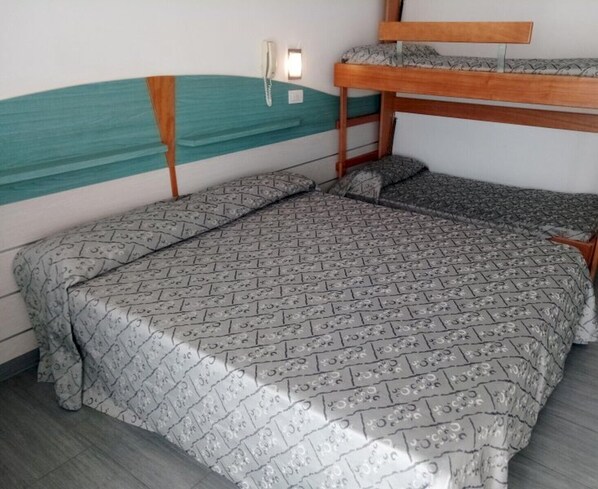 Una cama individual con una colcha estampada, un cabecero de madera, un teléfono en la pared y una ventana pequeña.