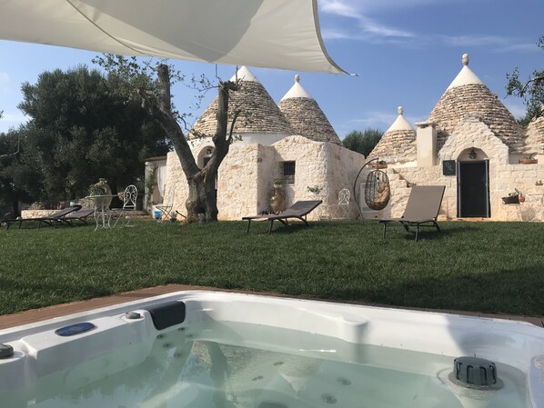 Un jacuzzi frente a un edificio de piedra con techos cónicos, mobiliario exterior y un árbol.
