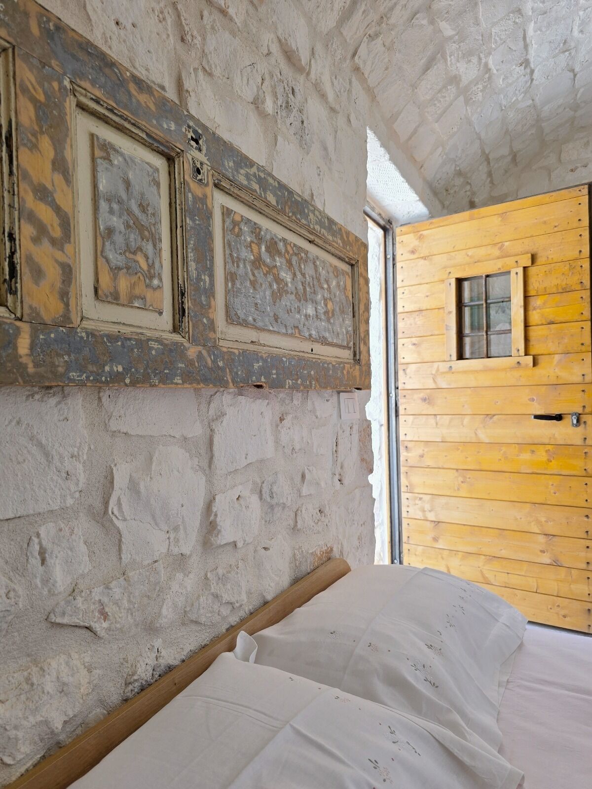Una habitación rústica con una cama, una puerta de madera y una pared de piedra.