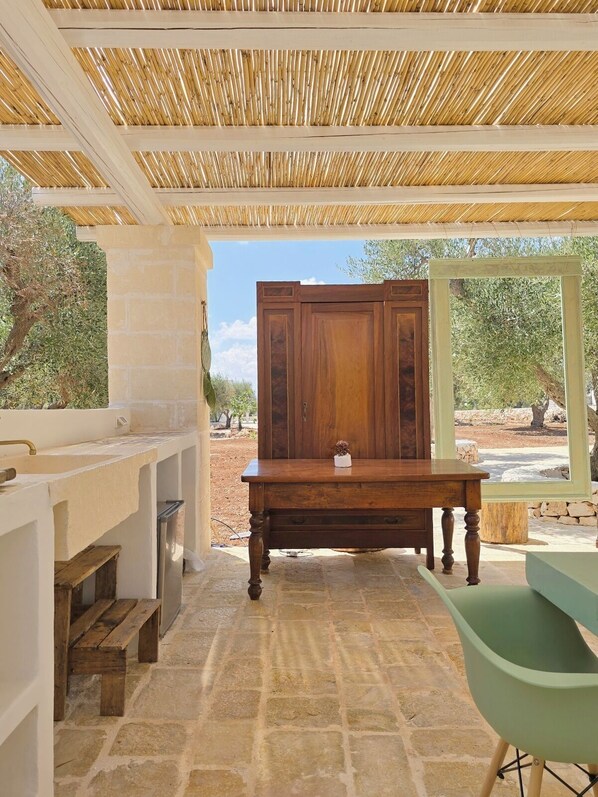 Un espacio al aire libre cubierto con suelo de piedra, una mesa de madera, un banco y una silla verde.