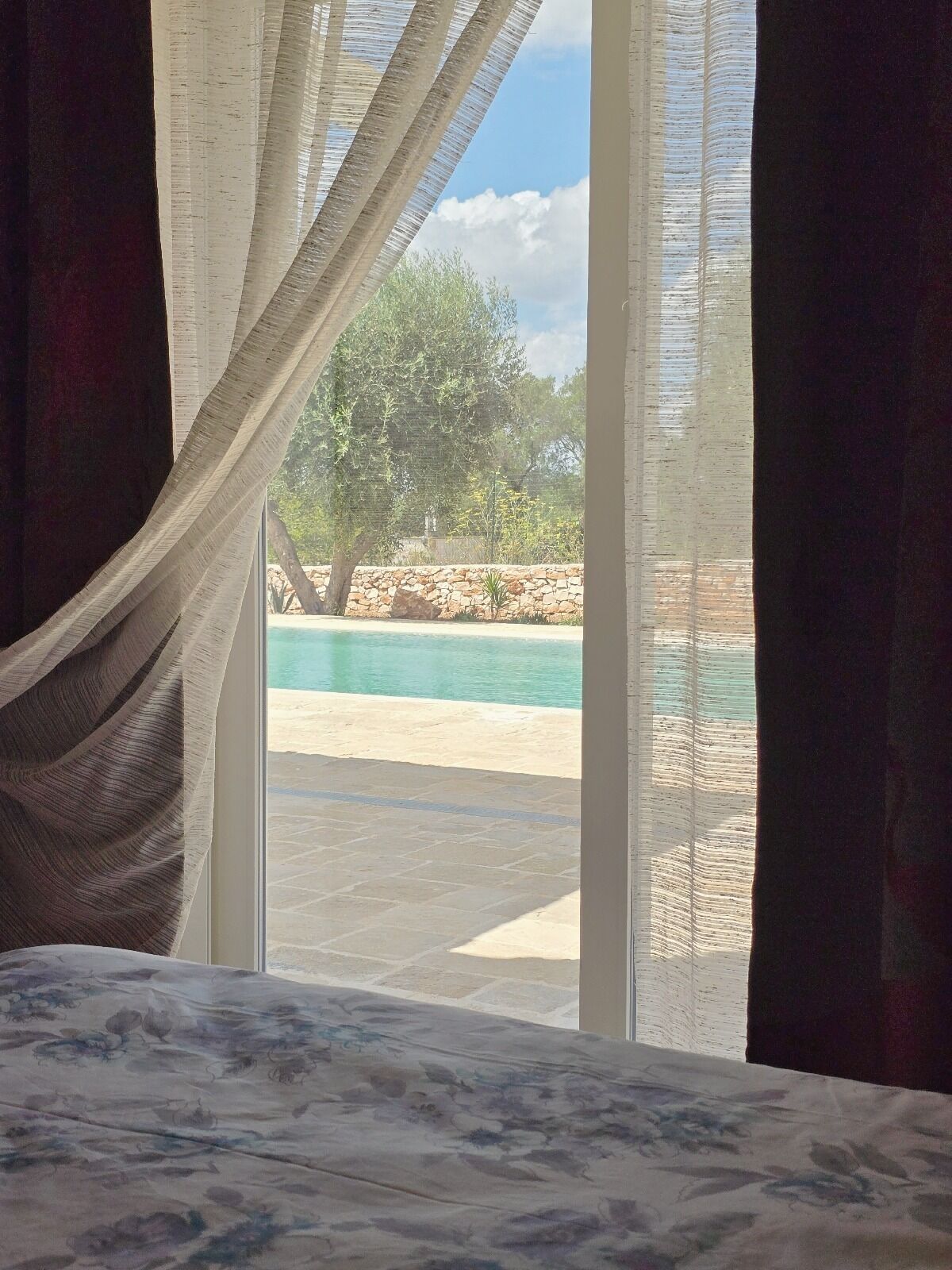 A bedroom with a view of a swimming pool and a stone wall.