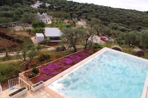 Una piscina con vista a una villa rodeada de olivos y un jardín con flores moradas.