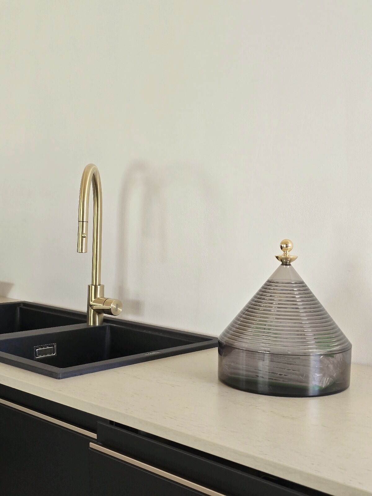 A kitchen with a black sink, a gold faucet, and a glass container with a metal lid on the countertop.
