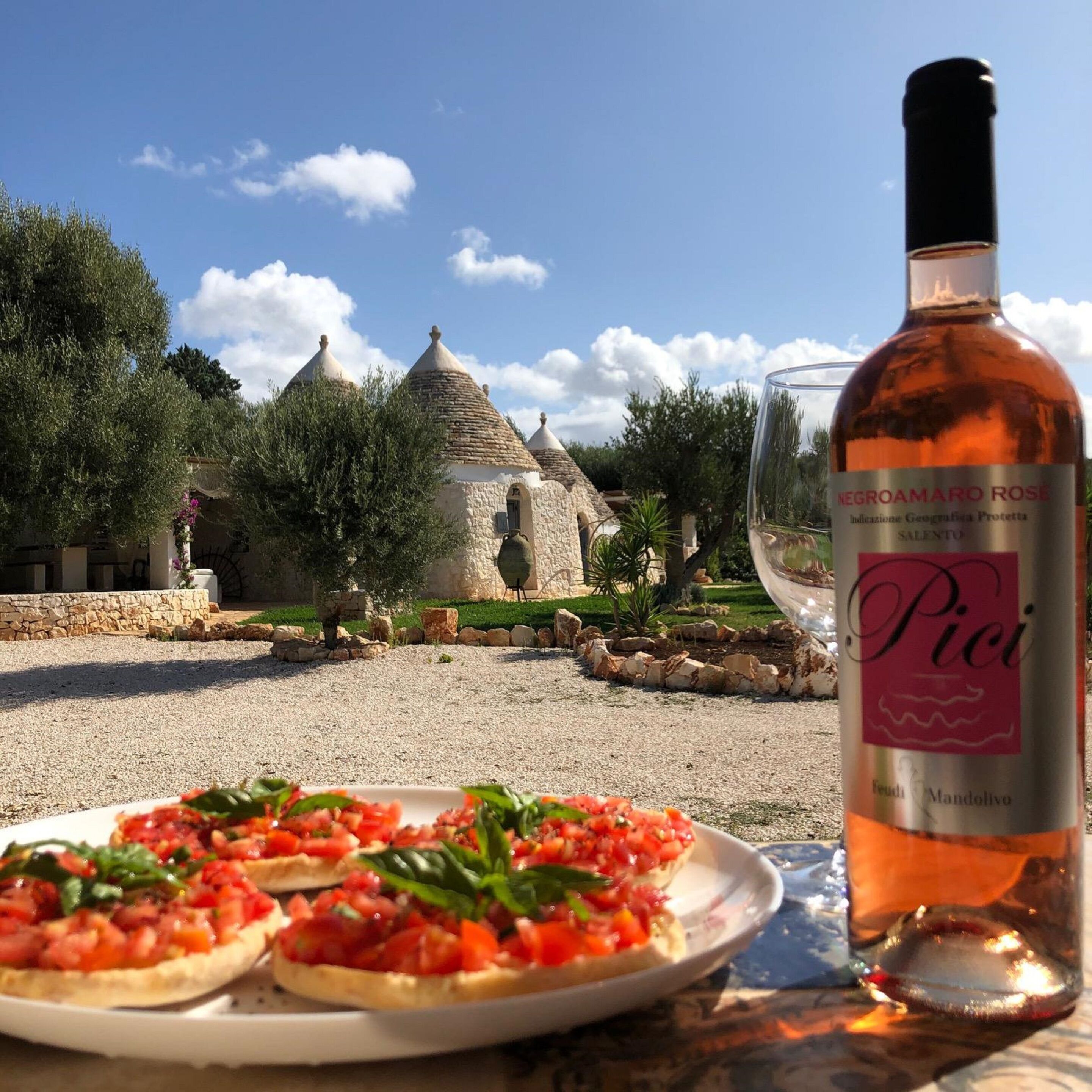 Uma mesa com bruschetta e uma garrafa de vinho em frente a um edifício de pedra com telhados pontudos.