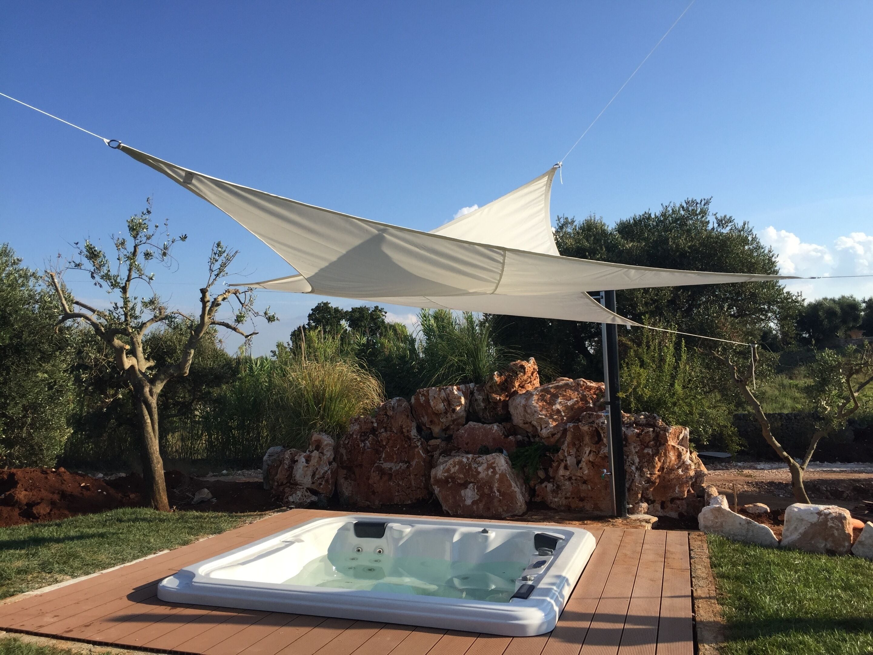 A hot tub on a wooden deck with a canopy overhead, surrounded by rocks and greenery.